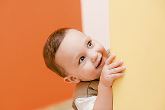 Happy Baby Boy Peeking from Behind Yellow Wall