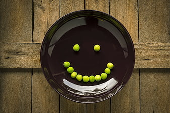 Creative smiley face made of green peas on a dark plate