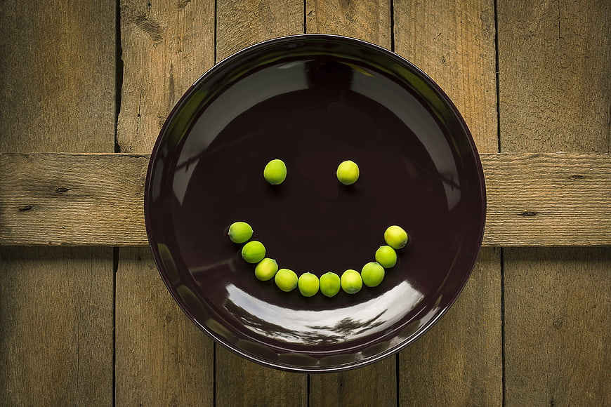Creative smiley face made of green peas on a dark plate