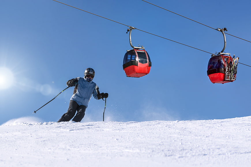 Skier on Slope with Red Gondola Lifts