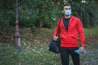 Man in Red Hoodie Walking in Park with Gym Bag and Mask