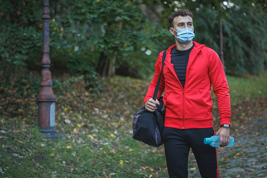 Man in Red Hoodie Walking in Park with Gym Bag and Mask