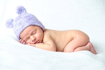 Sleeping newborn baby wearing purple knit hat on white blanket