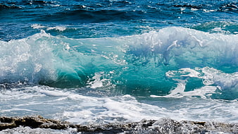 Powerful turquoise ocean wave crashing on rocky shore