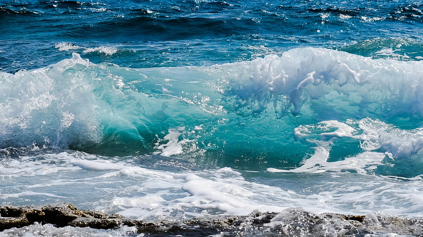 Powerful turquoise ocean wave crashing on rocky shore