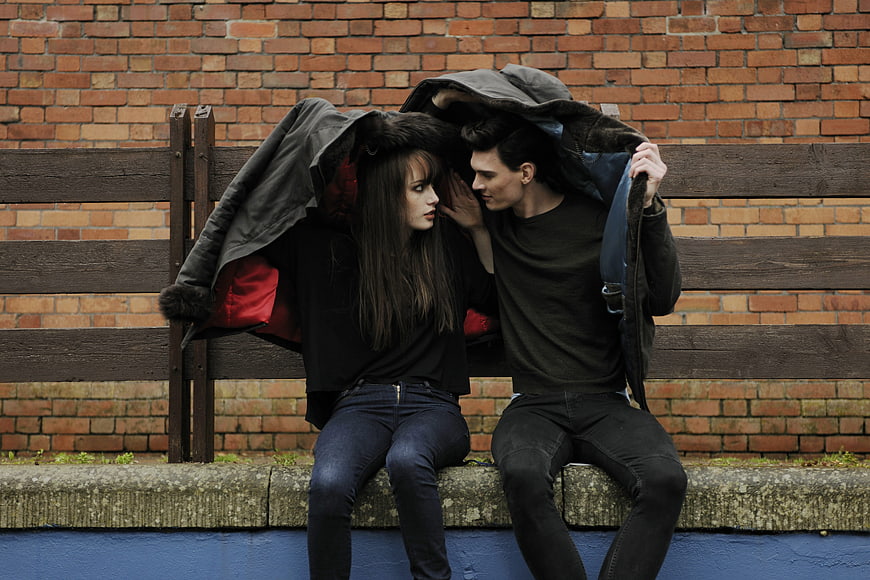 Young couple sharing jacket for shelter on bench