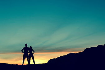 Silhouette of couple hiking on mountain ridge at sunset