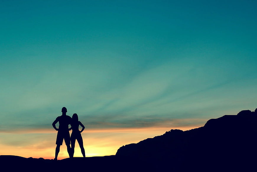 Silhouette of couple hiking on mountain ridge at sunset