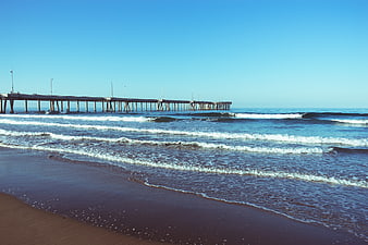 Long wooden pier extending over ocean waves on sunny beach