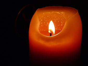 Close-up of a burning orange candle in the dark