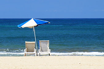 Blue and white beach umbrella with two lounge chairs on a sandy shore