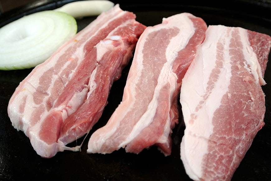 Raw pork belly slices and onion on a grill
