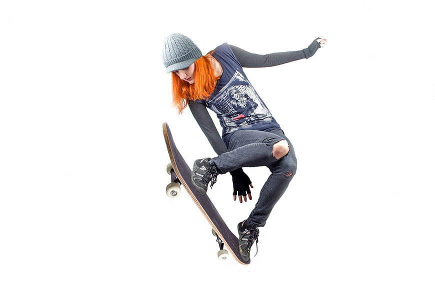 Young woman with orange hair skateboarding on white background