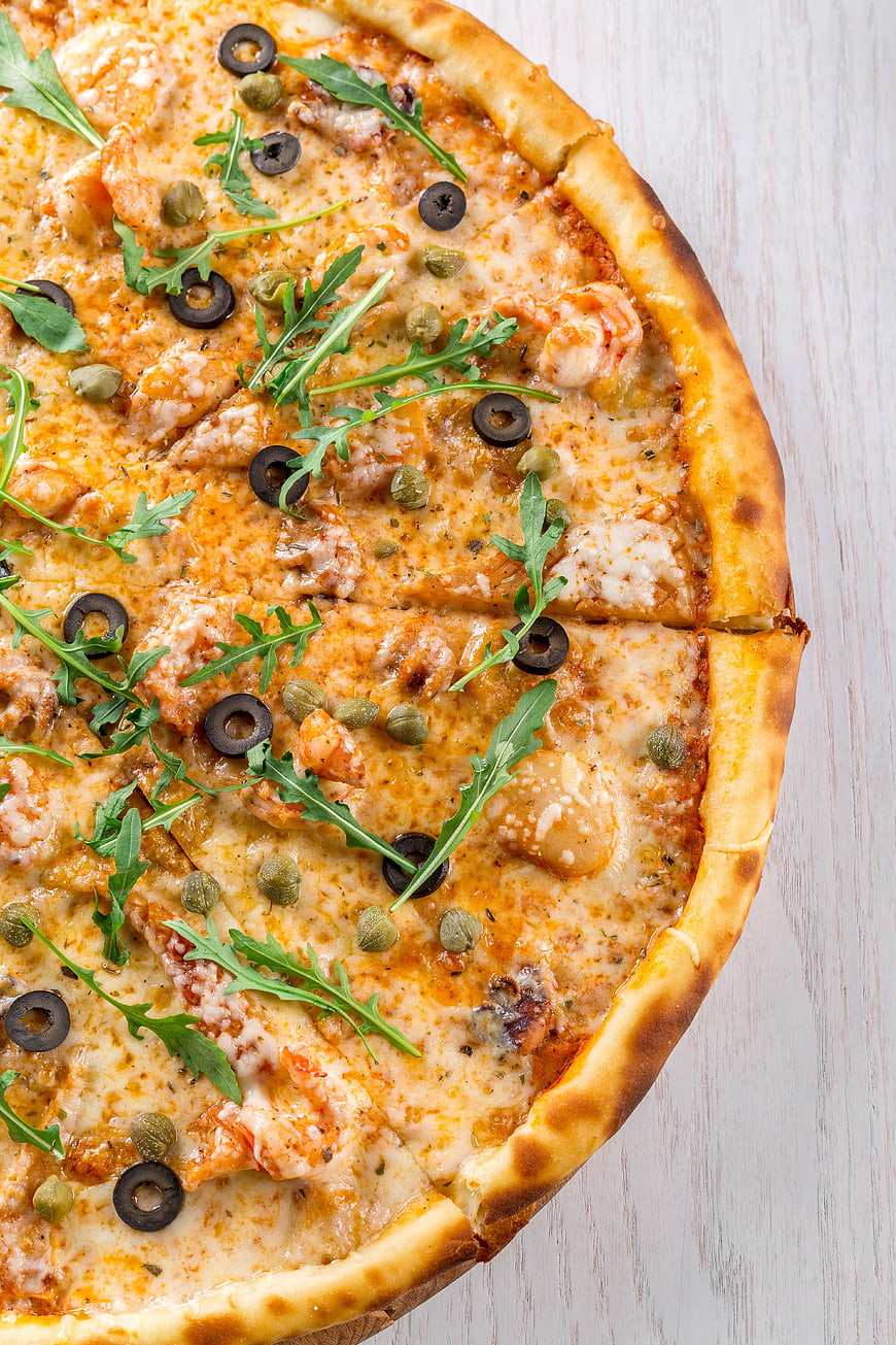 Overhead view of seafood pizza with arugula and olives