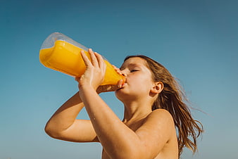 Young Girl Drinking Orange Juice Outdoors Against Blue Sky