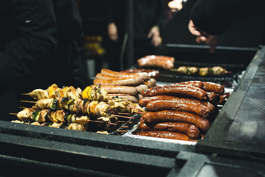 Grilled sausages and chicken skewers on a street food grill