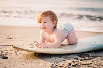 Happy baby boy lying on surfboard on sandy beach