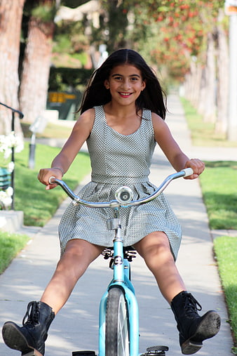 Smiling young girl riding a blue bicycle on a sunny suburban sidewalk