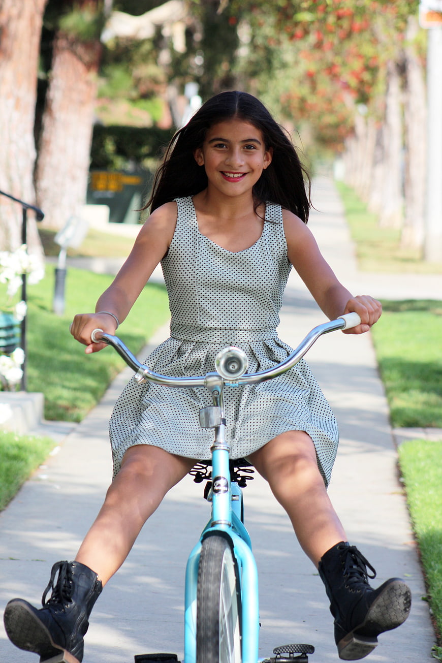 Smiling young girl riding a blue bicycle on a sunny suburban sidewalk