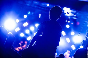 Silhouette of concertgoer with raised hand against blue stage lights