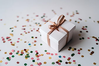 White gift box with gold ribbon and colorful confetti