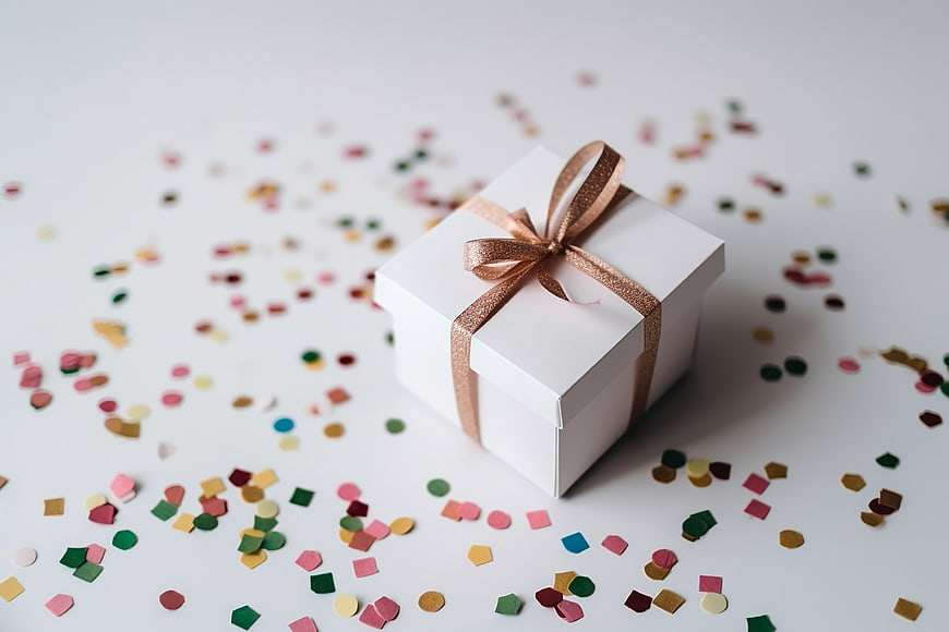 White gift box with gold ribbon and colorful confetti