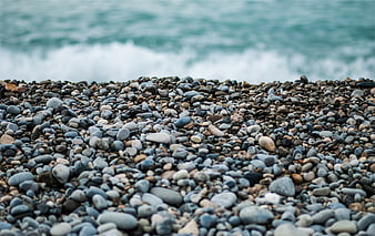 Close-up of smooth pebbles on a rocky beach with blurred ocean waves