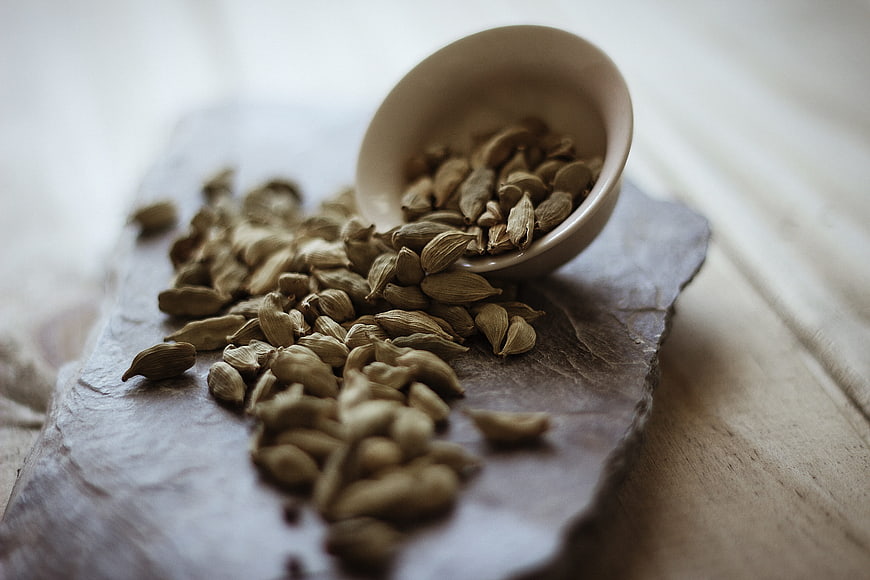 Cardamom Spilling from Ceramic Bowl on Slate