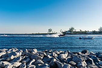 Speedboats racing through a sunny coastal inlet with rocky foreground