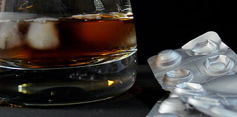 Glass of whiskey and blister pack of pills on black background
