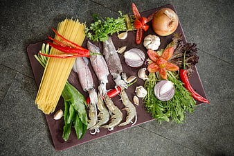 Fresh seafood and pasta ingredients on a dark cutting board