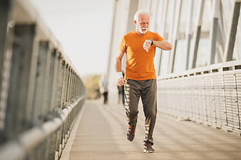 Senior man jogging on bridge checking smartwatch