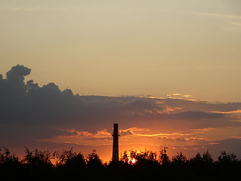 Silhouette of industrial chimney against dramatic sunset sky