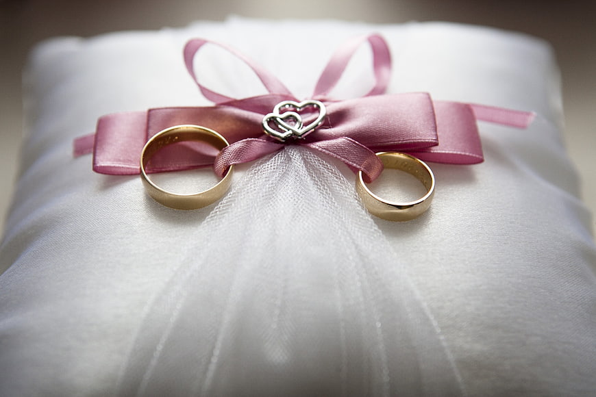 Gold wedding rings on white pillow with pink ribbon