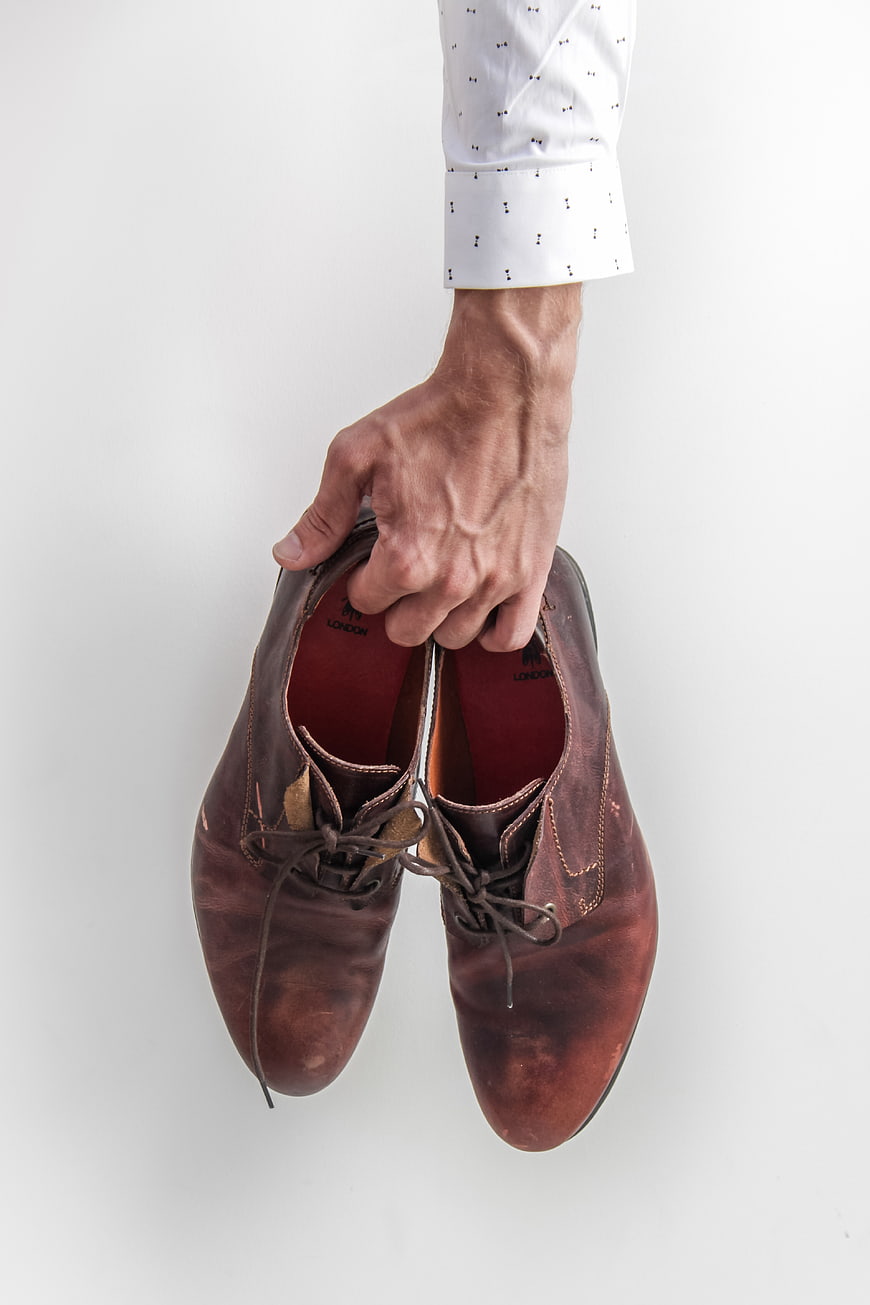 Man's Hand Holding Brown Leather Shoes
