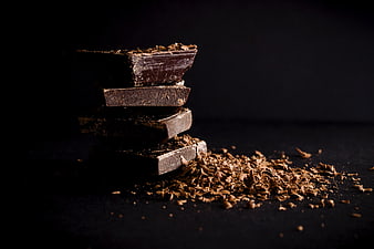 Stack of dark chocolate pieces with shavings on black background
