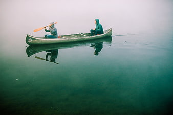Two men canoeing on a misty lake at dawn