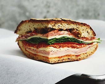 Close-up of a layered deli sandwich with ham, cheese, and greens