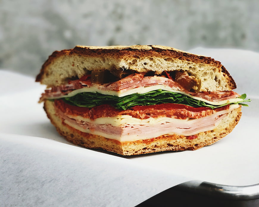 Close-up of a layered deli sandwich with ham, cheese, and greens