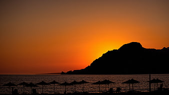 Silhouette of Beach Umbrellas Against Vibrant Orange Sunset Sky