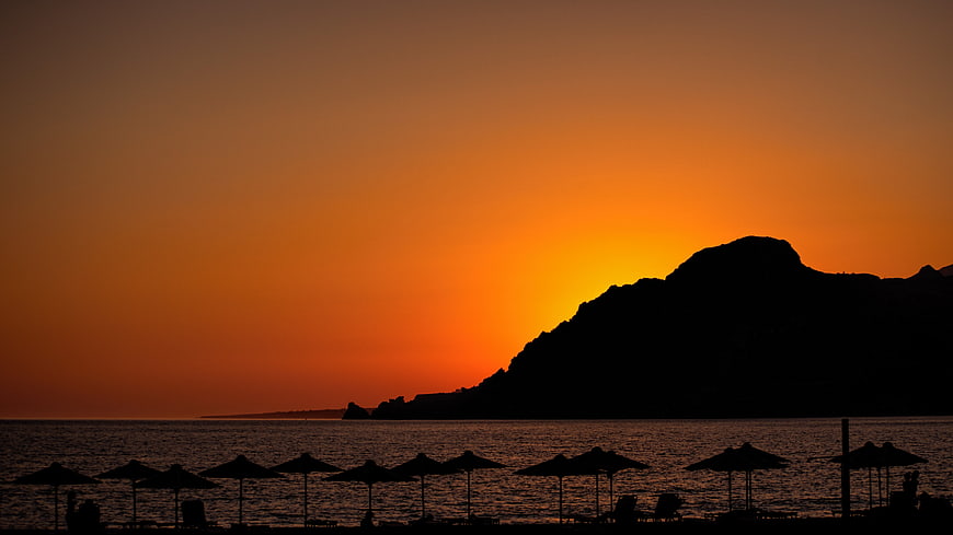 Silhouette of Beach Umbrellas Against Vibrant Orange Sunset Sky
