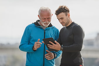Senior man and young trainer reviewing fitness tablet outdoors