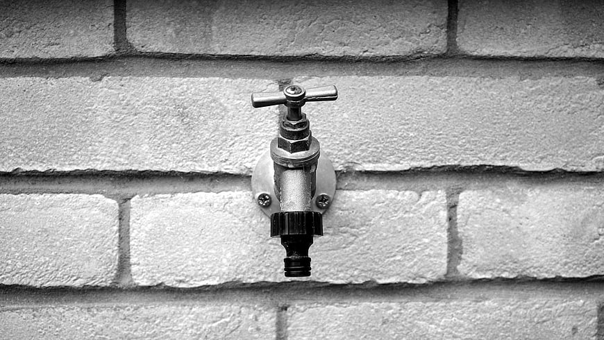 Black and white outdoor faucet on brick wall