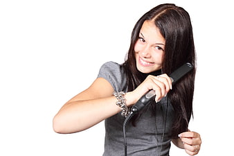 Happy young woman using hair straightener on white background
