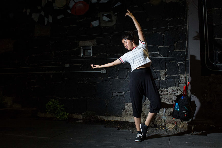 Young woman dancing at night against stone wall