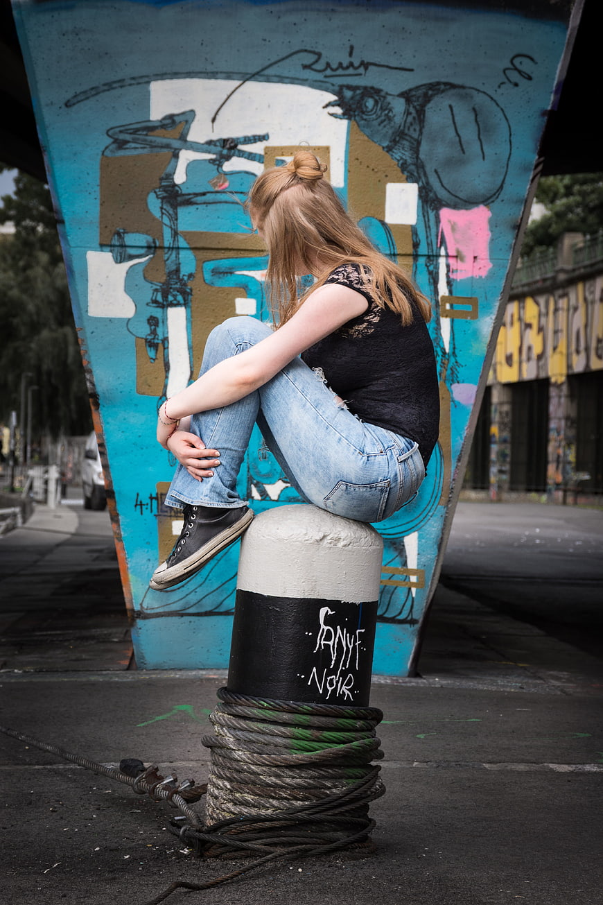 Sad teenage girl sitting on bollard against graffiti wall
