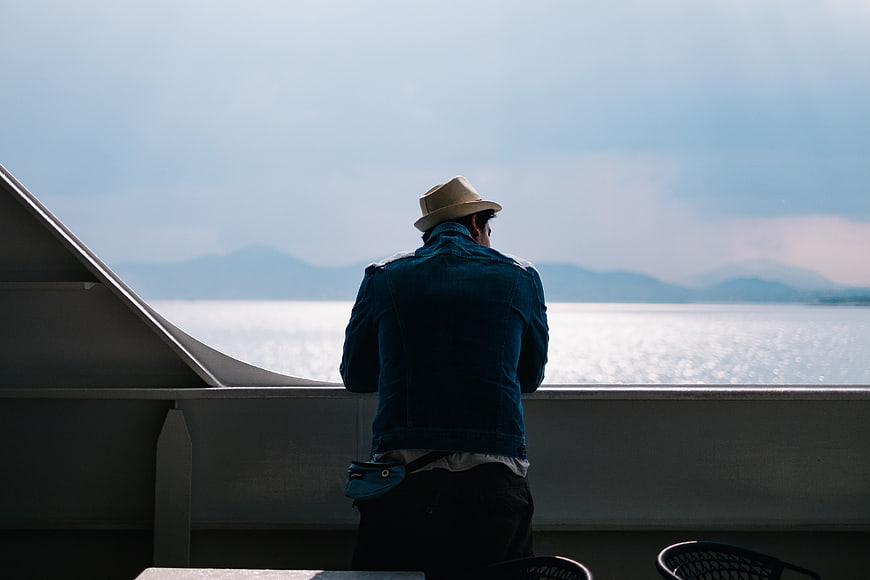 Man in hat looking out at ocean from ship deck