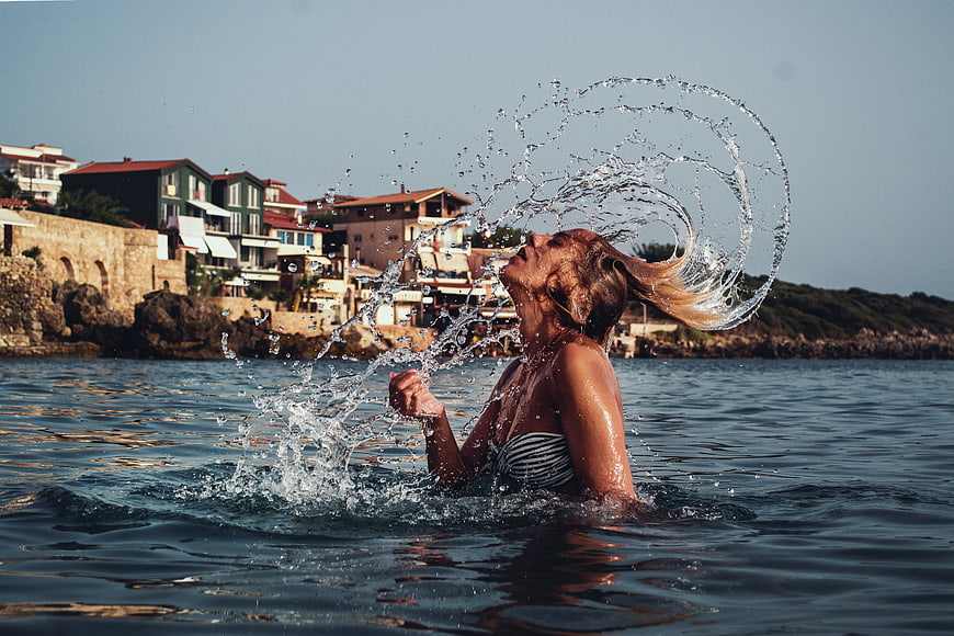 Woman Splashing Water in Sea with Coastal Village Background