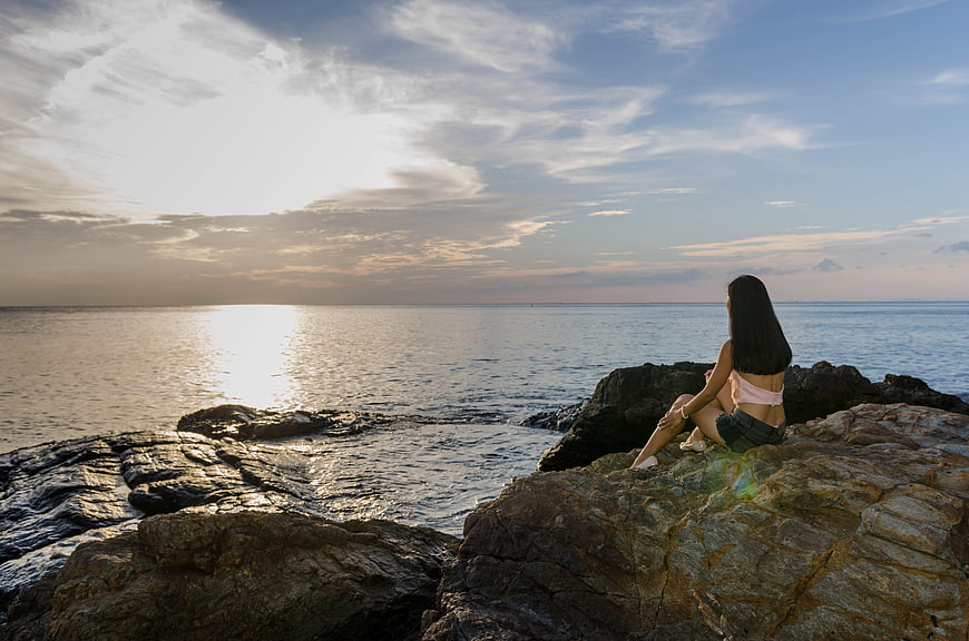 Young Woman Sitting on Rocky Shore at Sunset