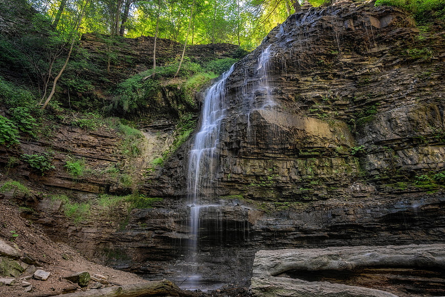 Tall waterfall cascading down layered rock cliff in forest